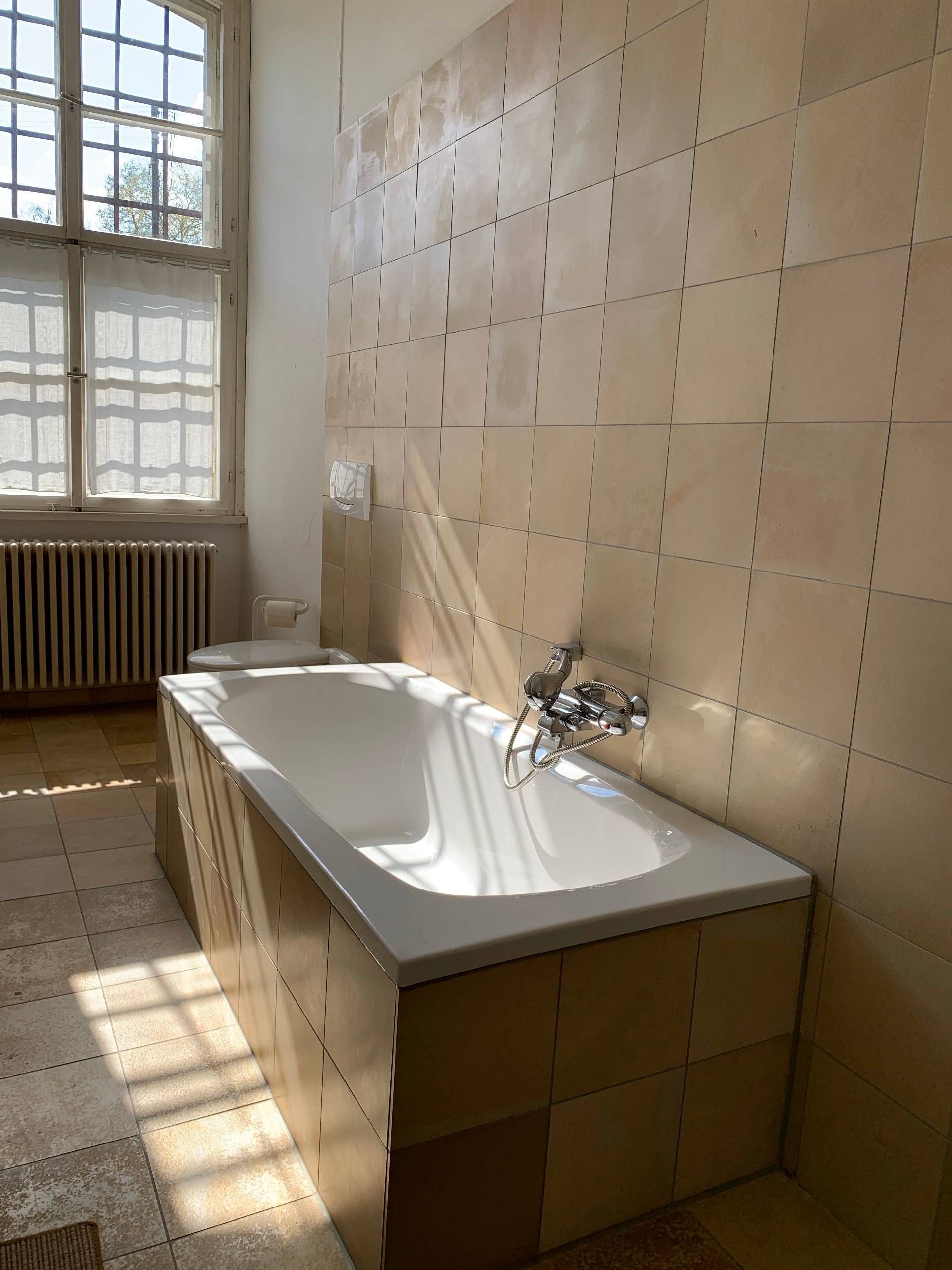 Ein Badezimmer mit einer Badewanne, einem Fenster und einer Heizung.