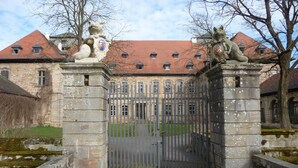 A historic building with a gated entrance, stone statues, and a red-tiled roof. - Ferienzimmer im Schloss Burgpreppach (Burgpreppach)