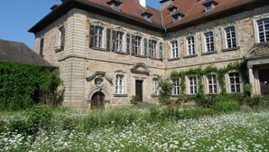 A historic stone building with multiple windows and a garden in front. - Ferienzimmer im Schloss Burgpreppach (Burgpreppach)