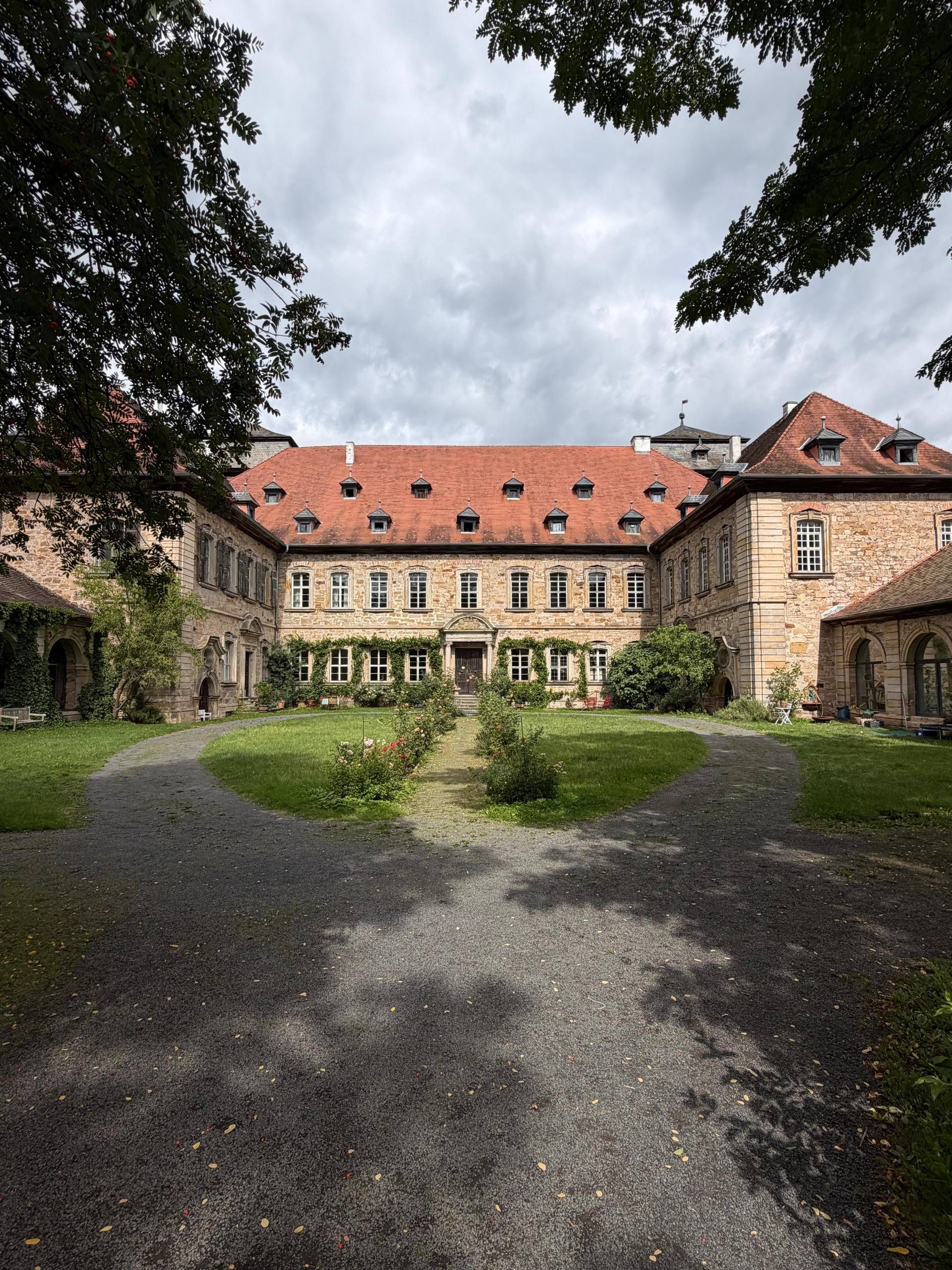 A courtyard with a central pathway leading to a building with a red-tiled roof and stone walls.