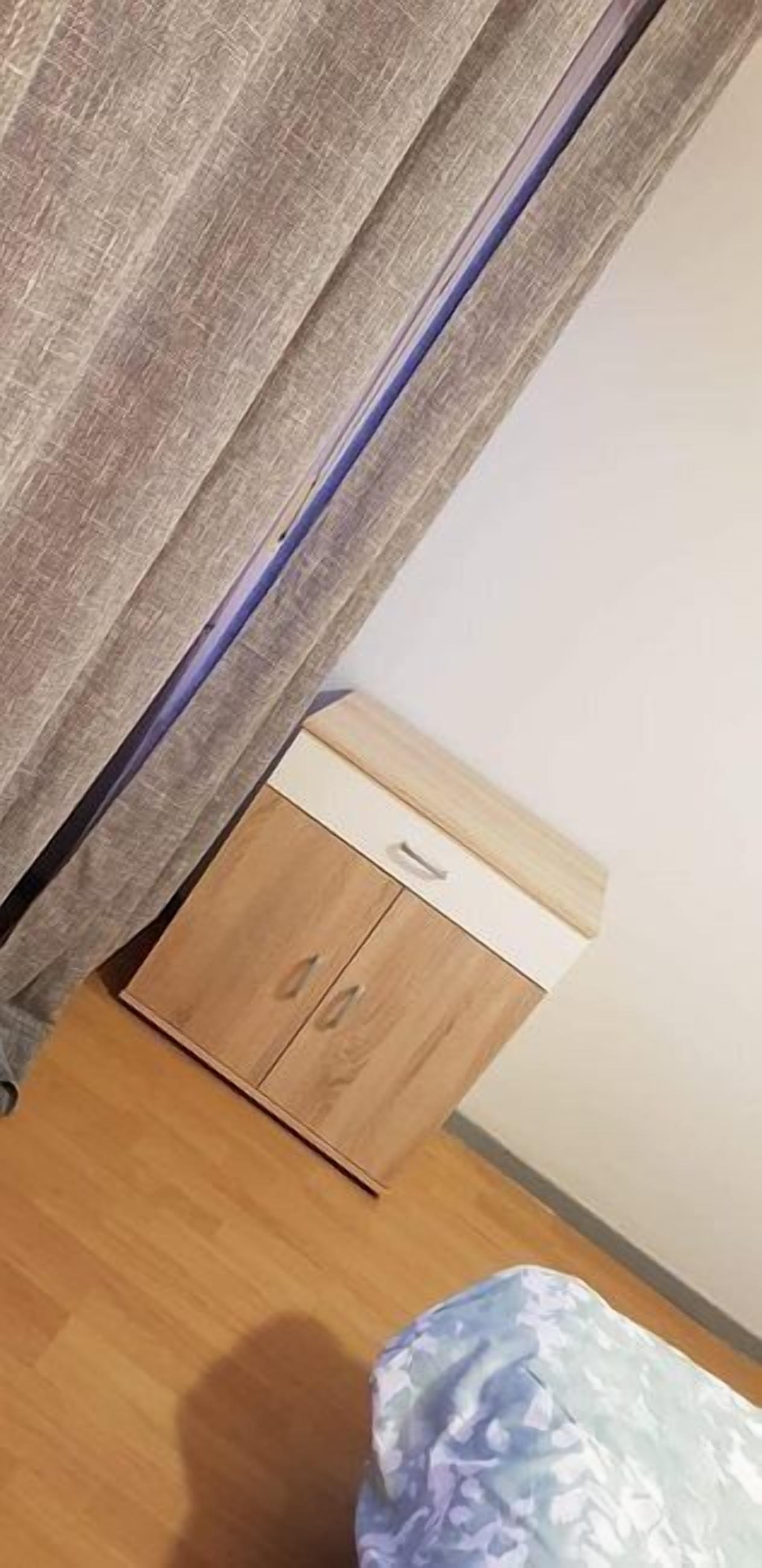 Un dormitorio con un armario de madera, una cama con edredón estampado y una cortina entreabierta.