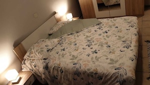 Un llit ben fet amb roba de llit floral, una làmpada de nit i un panell de capçal de fusta.