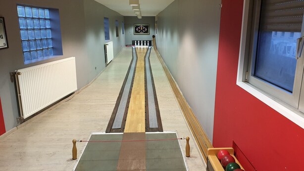Una bolera amb una pista verda, claus de fusta i un suport vermell per a les boles.