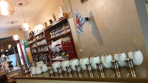 Zona de bar amb prestatges plens de botelles i vasos, una màquina de cafè i una fila de tasses de ceràmica blanca al taulell.