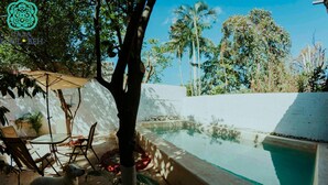 Un área de piscina con un muro blanco, un árbol y un perro.