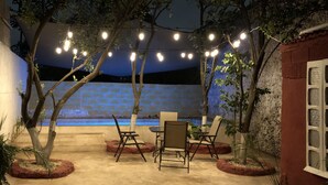 Un patio al aire libre con luces colgantes, un muro de ladrillo y asientos.