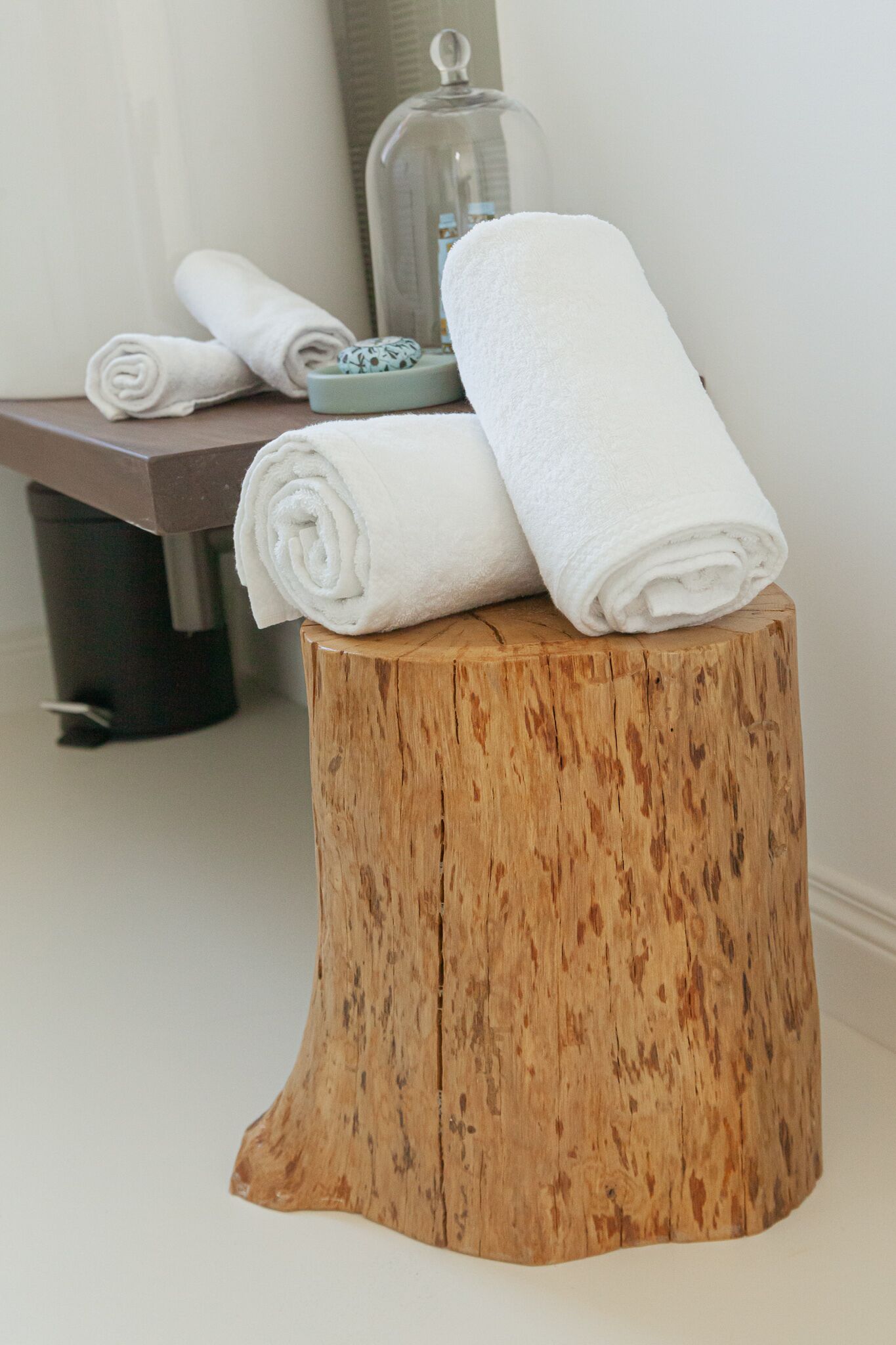 A wooden stool with rolled white towels and a glass container with a lid.