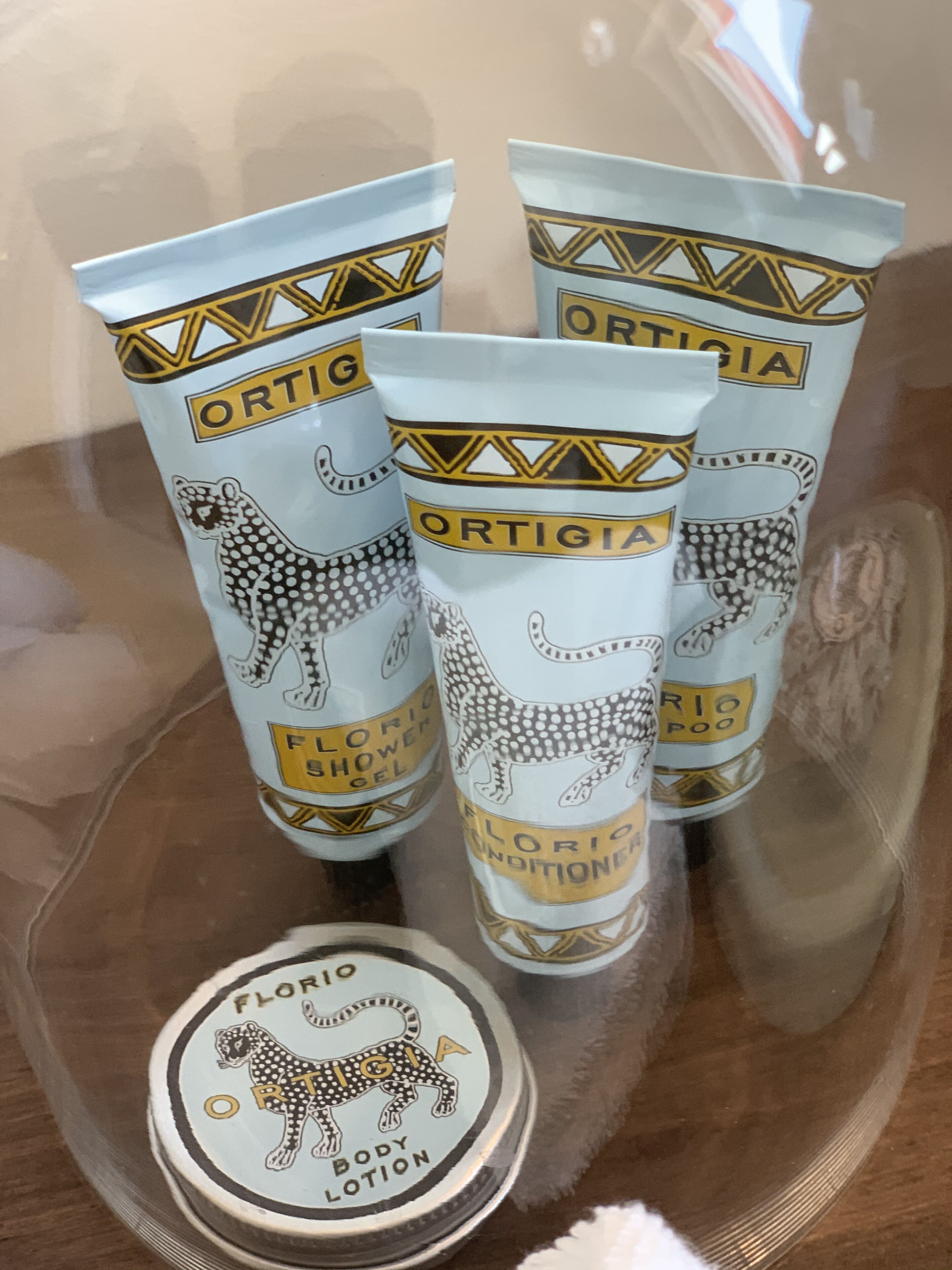 Cuatro tubos de loción corporal y un tubo de gel de ducha sobre una superficie reflectante.