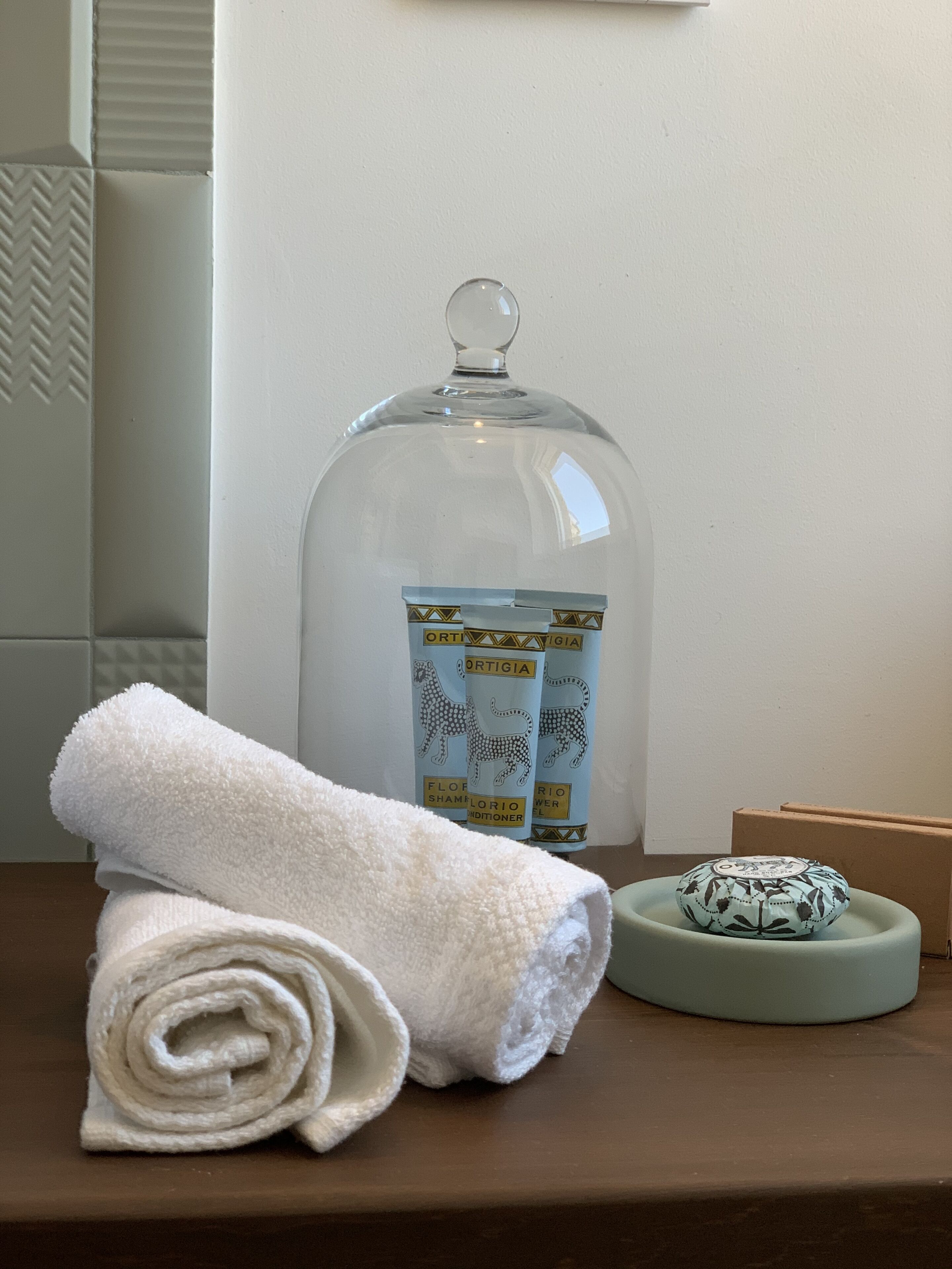 Un baño con una toalla, un recipiente de vidrio con etiqueta y un jabonera.