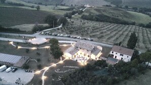 An aerial view of a rural property with a large building surrounded by parked cars, a winding path, and fields. - Frantoio L'Olinda (San Marcello)