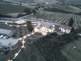 An aerial view of a rural property with a large building surrounded by parked cars, a winding path, and fields.