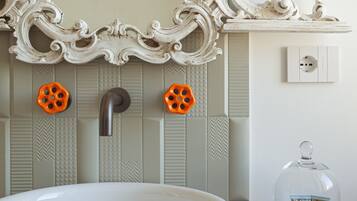 Un baño con lavamanos blanco, espejo decorativo y mandos de ducha anaranjados.