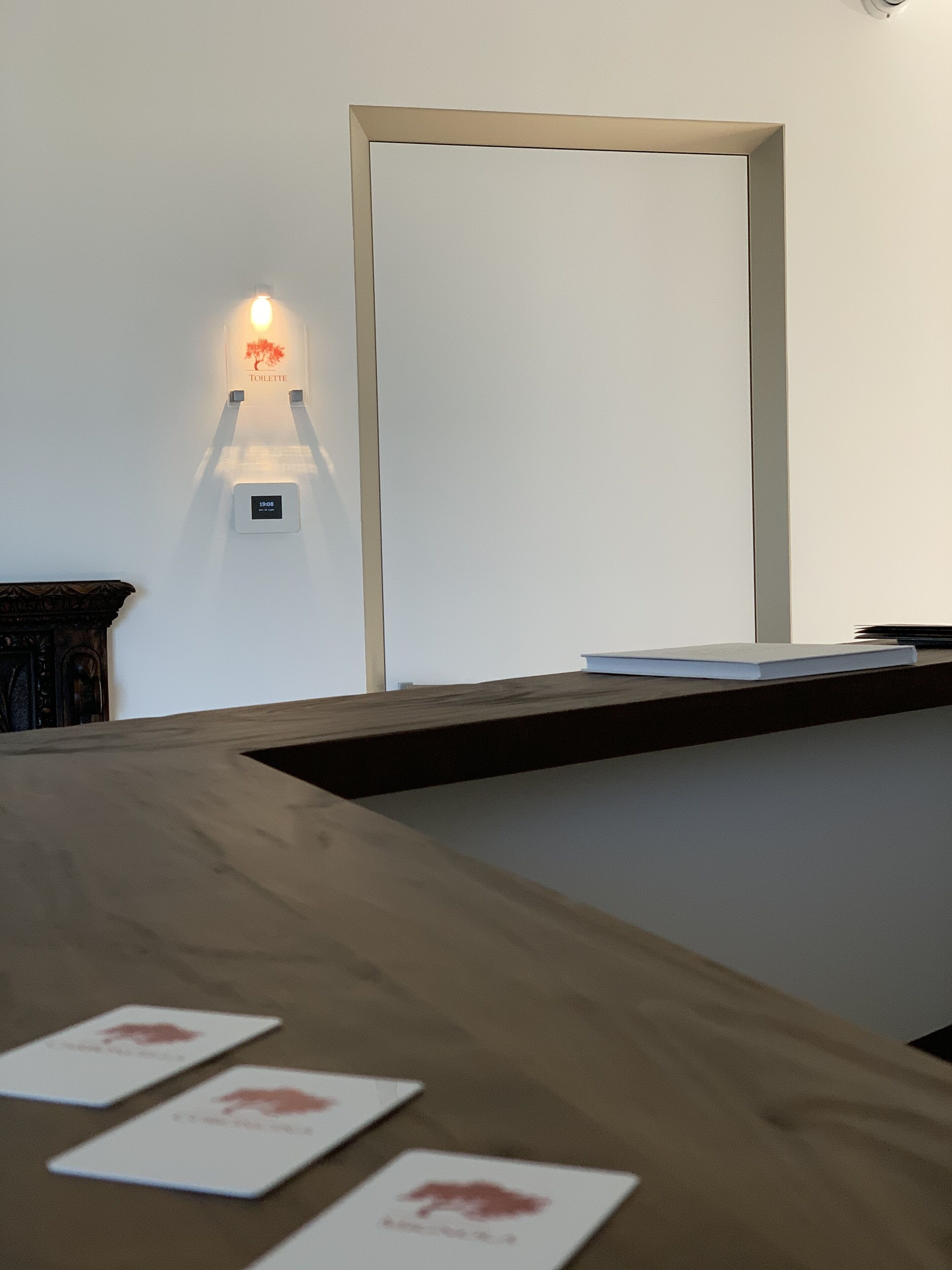 Bancada de recepção com superfície de madeira, um espelho emoldurado e luminária fixada na parede.