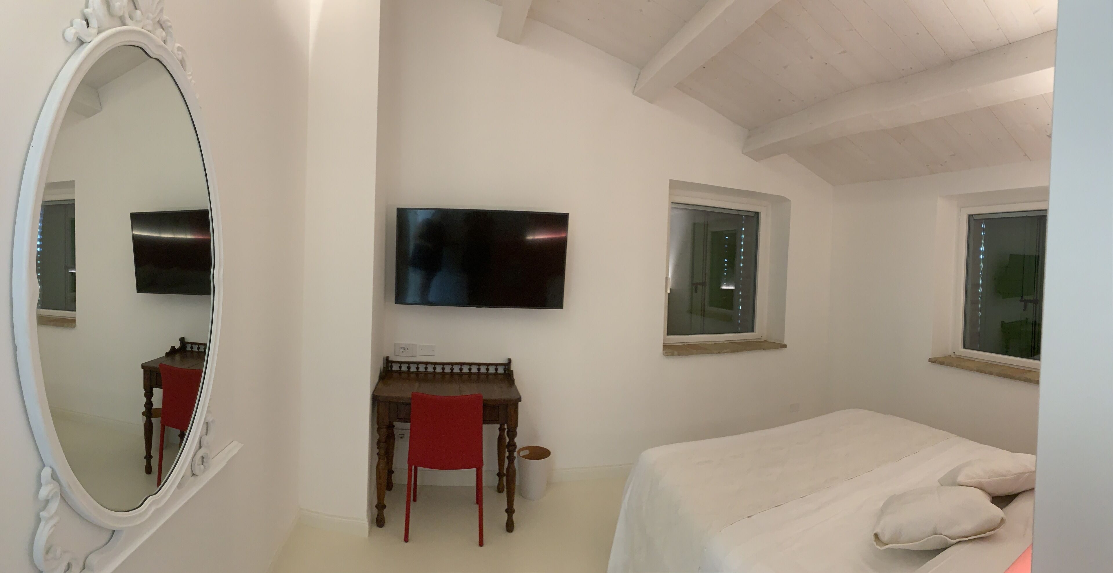 A bedroom with a bed, a desk with a chair, a TV, and two windows.