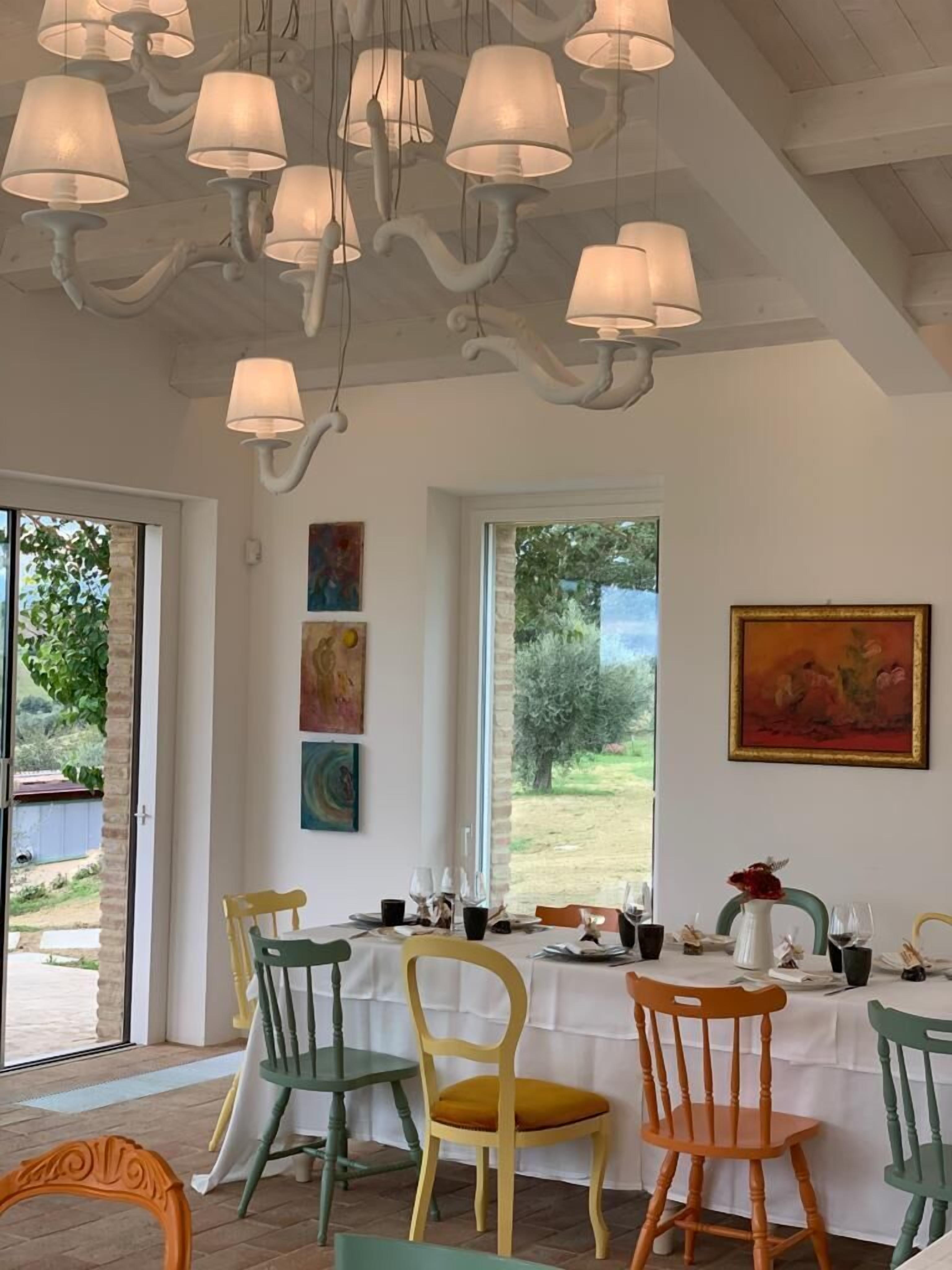 A dining area with a table set for four, surrounded by colorful chairs, a ceiling with hanging lamps, and artwork on the walls.