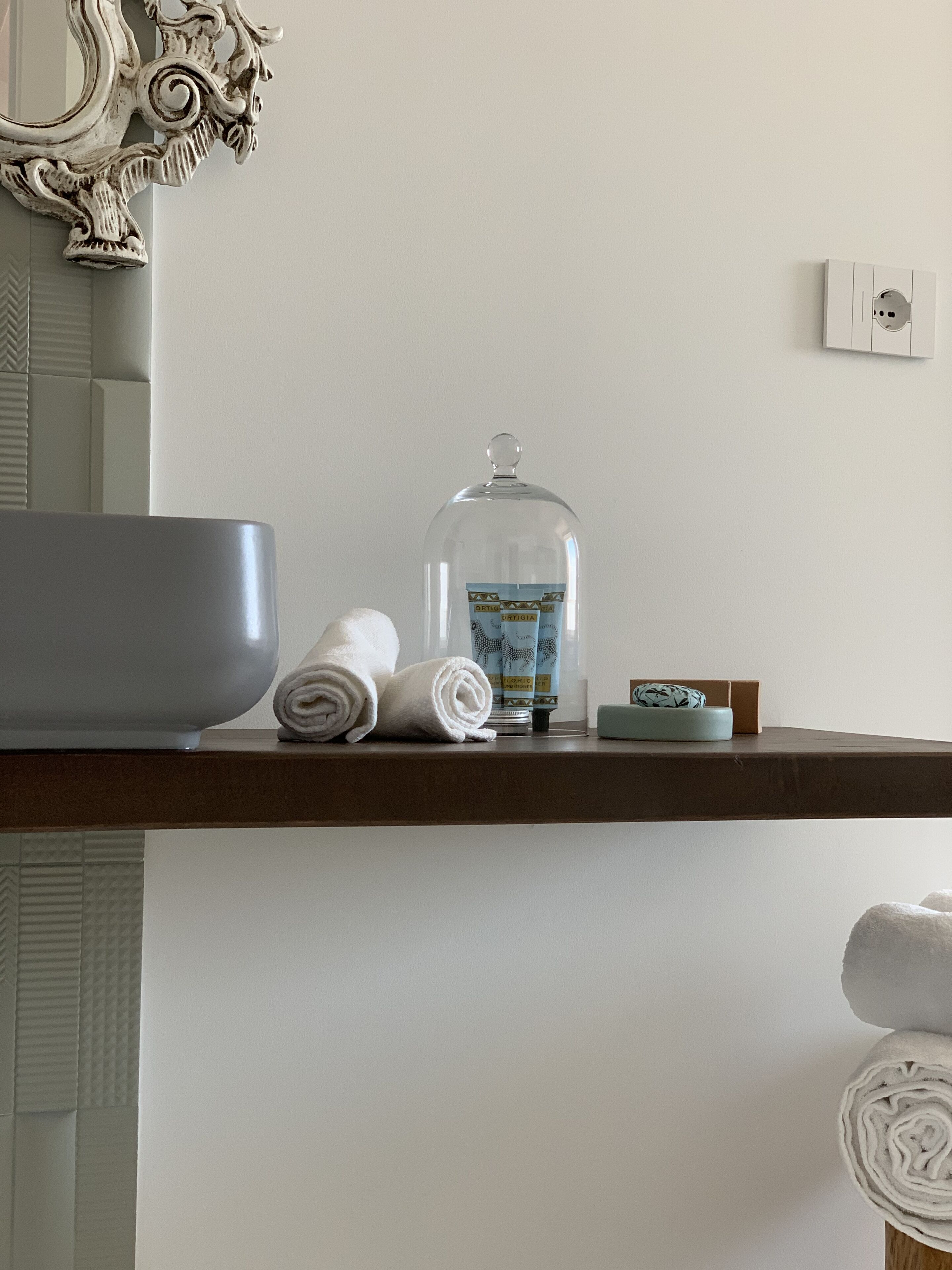 Un baño con un espejo grande, un lavabo, un perchero para toallas y un dispensador de jabón en la encimera.