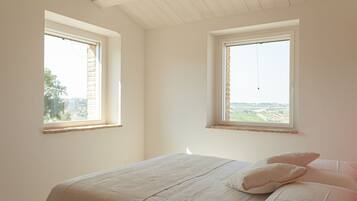 Une chambre avec deux fenêtres, un lit avec des oreillers et une vue sur la campagne.