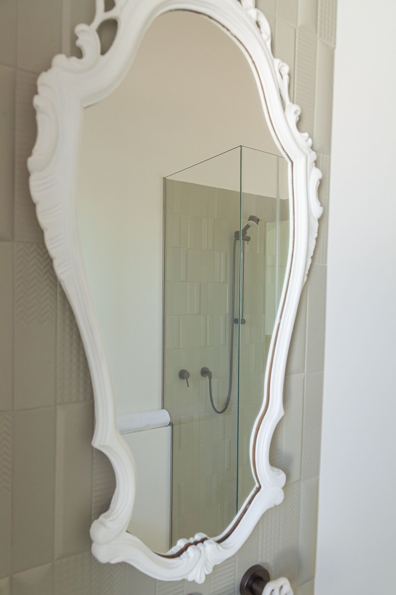 Un baño con un espejo grande y ornamentado, una ducha con cerramiento de vidrio y un revestimiento de azulejos.