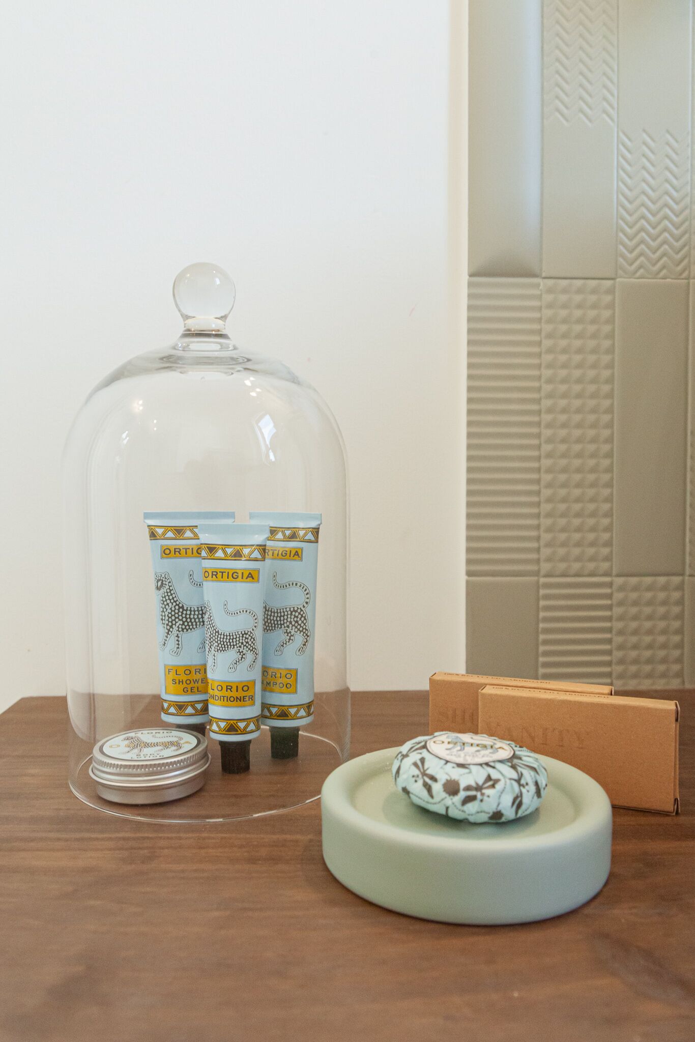 Un meuble-lavabo de salle de bain avec un porte-savon en verre transparent pour la douche, deux bouteilles de gel douche, un petit récipient rond pour le savon et une boîte de papier toilette.