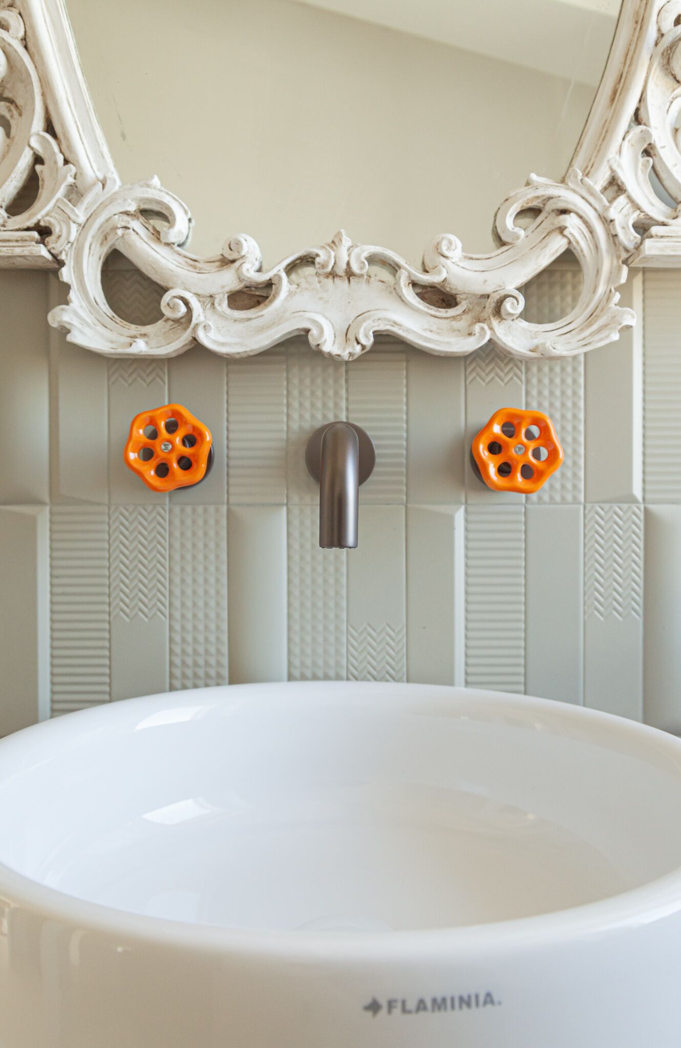 A bathroom with a white sink, a mirror with ornate detailing, and two orange soap dispensers.