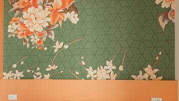 A bed with white bedding in a room with orange walls and a large floral-patterned wall hanging above it.