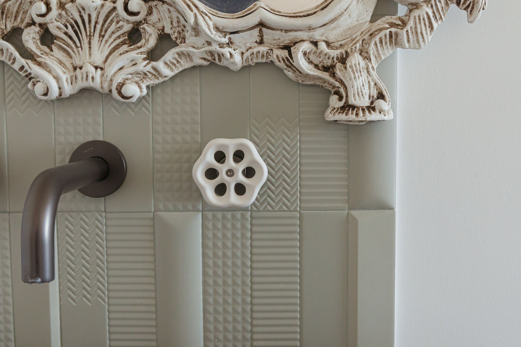 A bathroom with a decorative wall panel, a modern faucet, and a unique sink design.