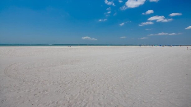 A wide sandy beach with a clear blue sky and a few scattered clouds.