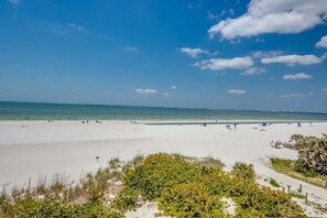 Une plage avec un ciel dégagé, un rivage sablonneux et une végétation clairsemée.
