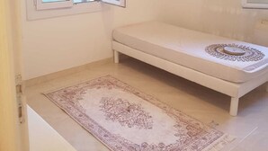 Een kleine, schone kamer met een enkel bed, een raam en een kamerkleed met een patroon.