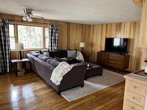 Een gezellige woonkamer met een donkerbruine bank, een flatscreen televisie, houten lambrisering en een plafondventilator.