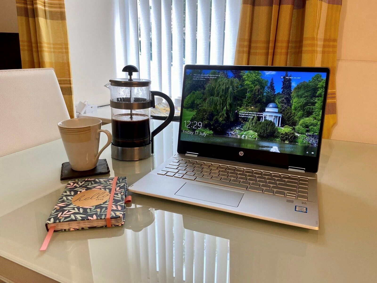 Un ordinateur portable est posé sur une table, à côté d’une machine à café, d’une tasse et d’un carnet.