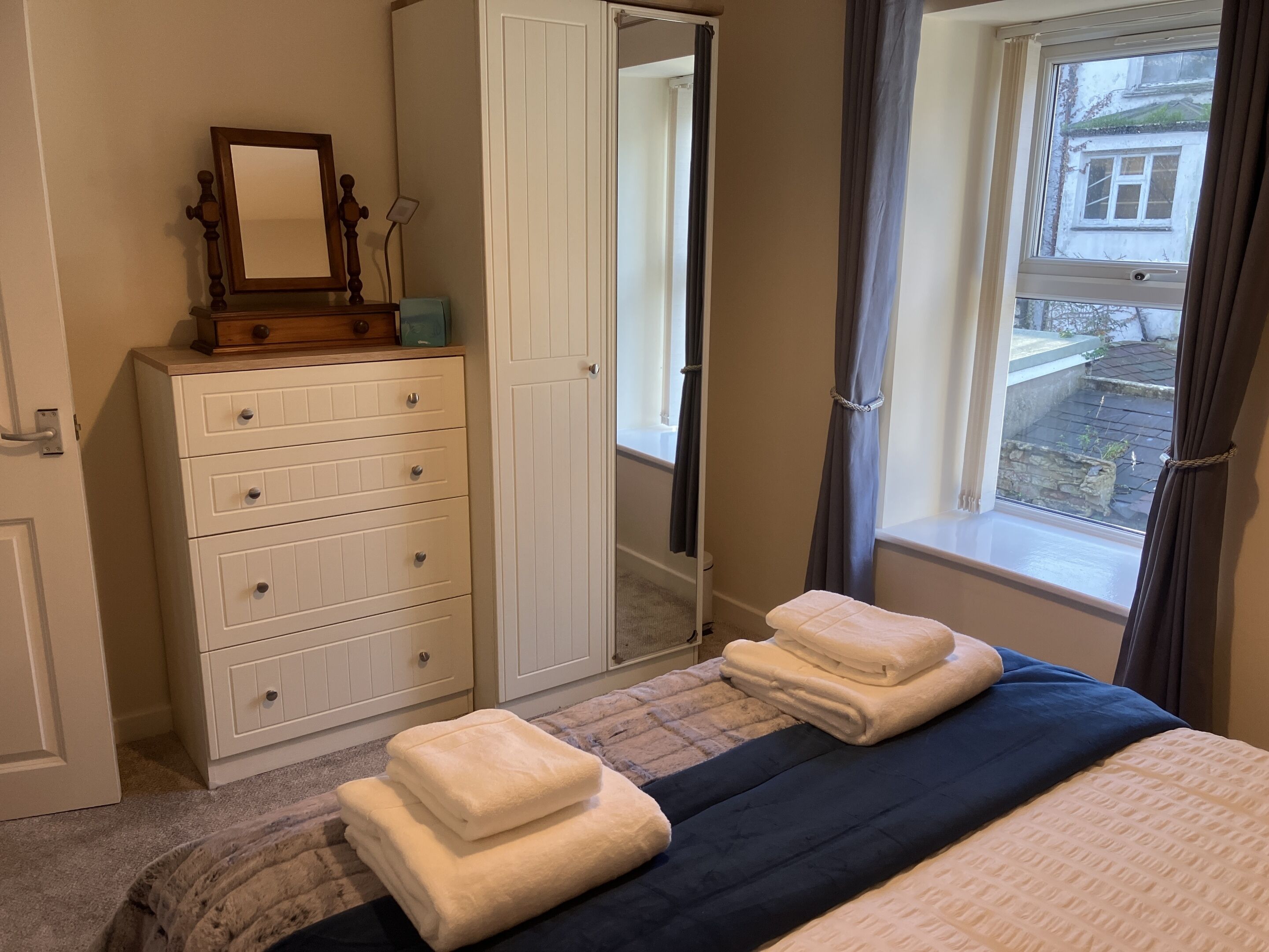A bedroom with a bed, a dresser, a mirror, and a window with curtains.
