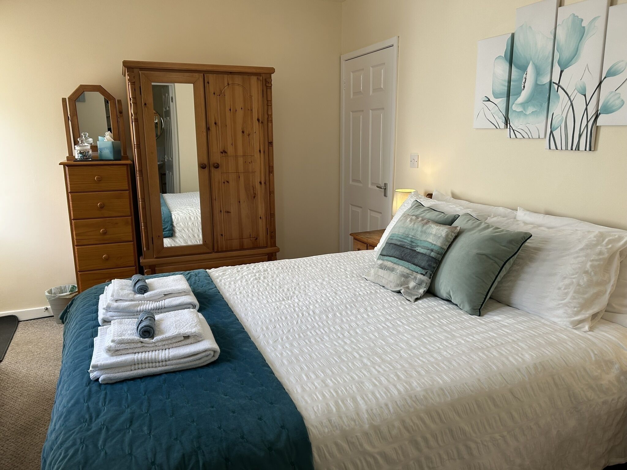 A bedroom with a bed, a wooden wardrobe, a mirror, and artwork on the wall.