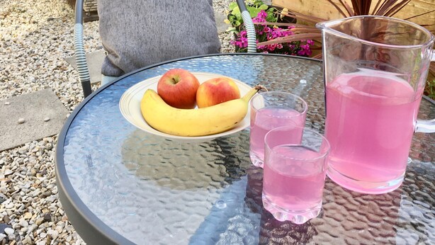 A table with a plate of fruit, two glasses of pink drink, and a potted plant. - Chapel St Apartments (Caernarfon)