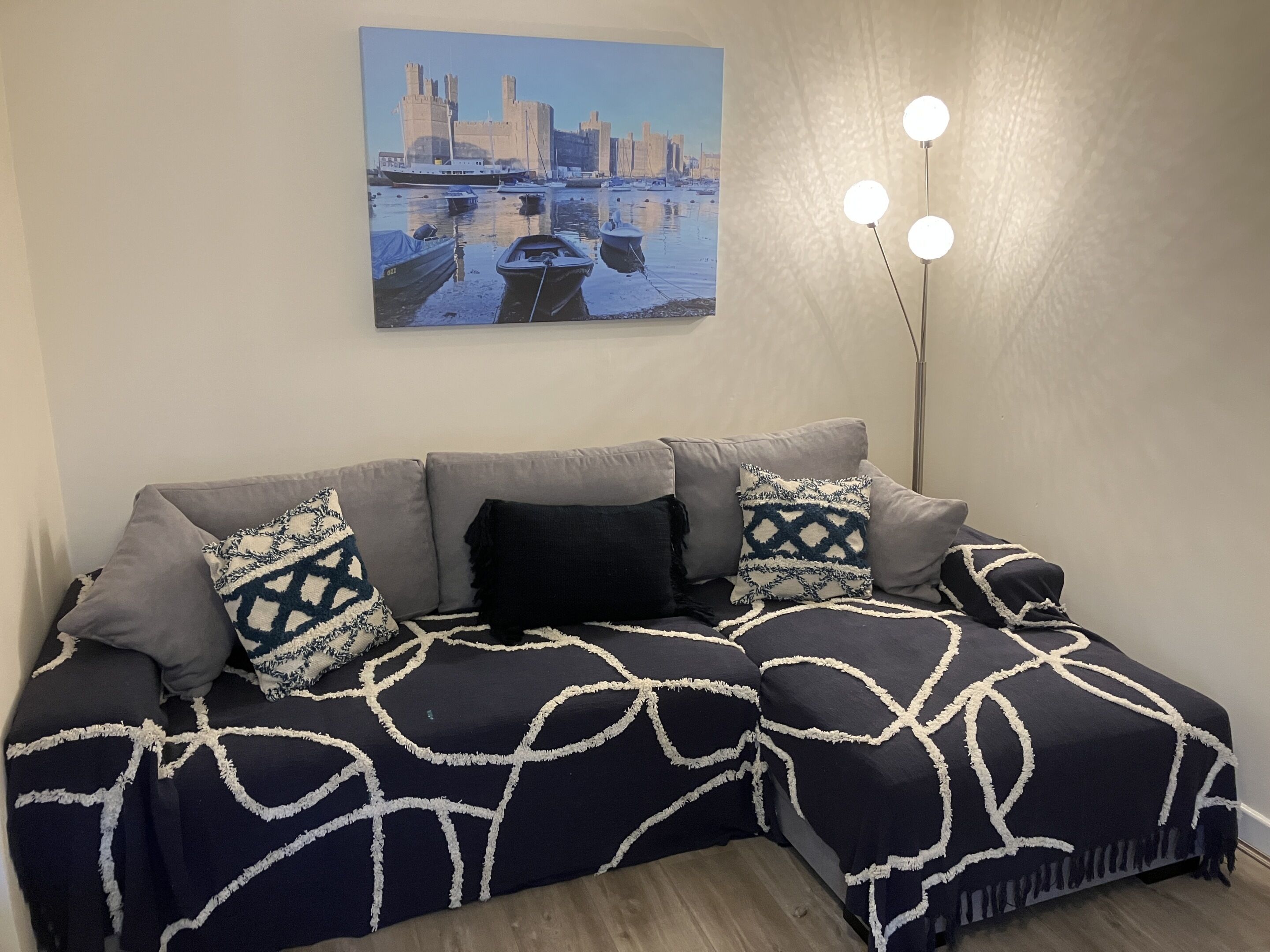 Un salon moderne avec un canapé d’angle, un tableau représentant un paysage urbain et une lampe sur pied.