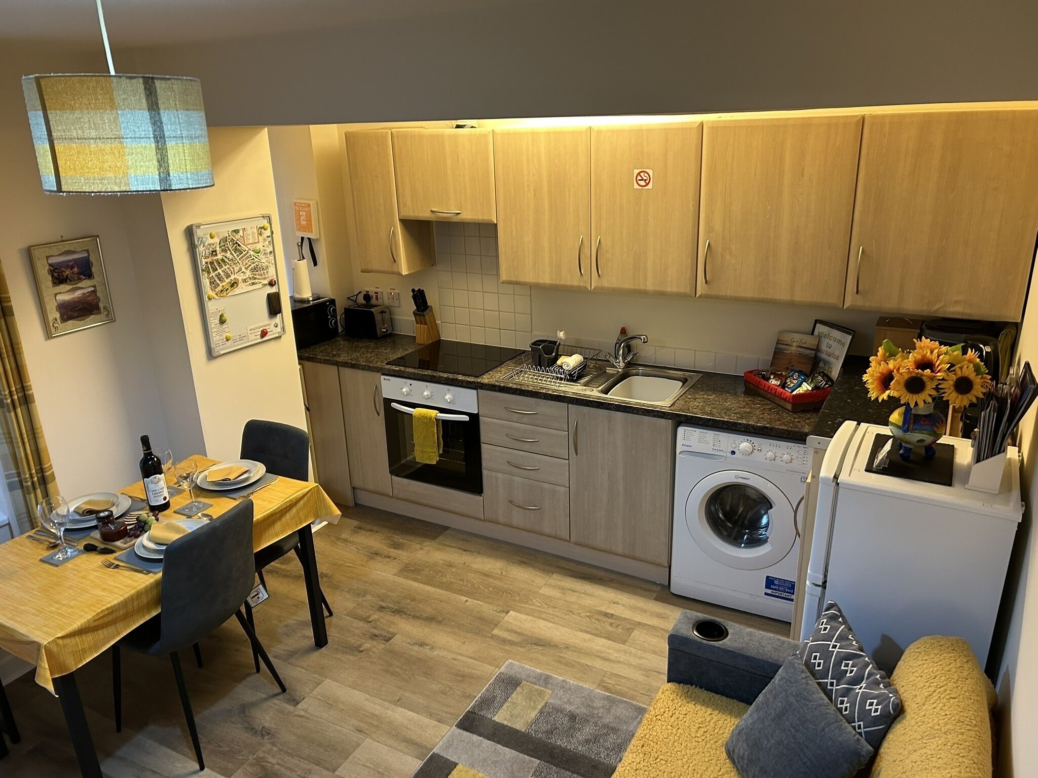 Een praktische keuken met houten kastjes, een inbouwoven, een wasmachine en een eethoek met een tafel voor twee personen.
