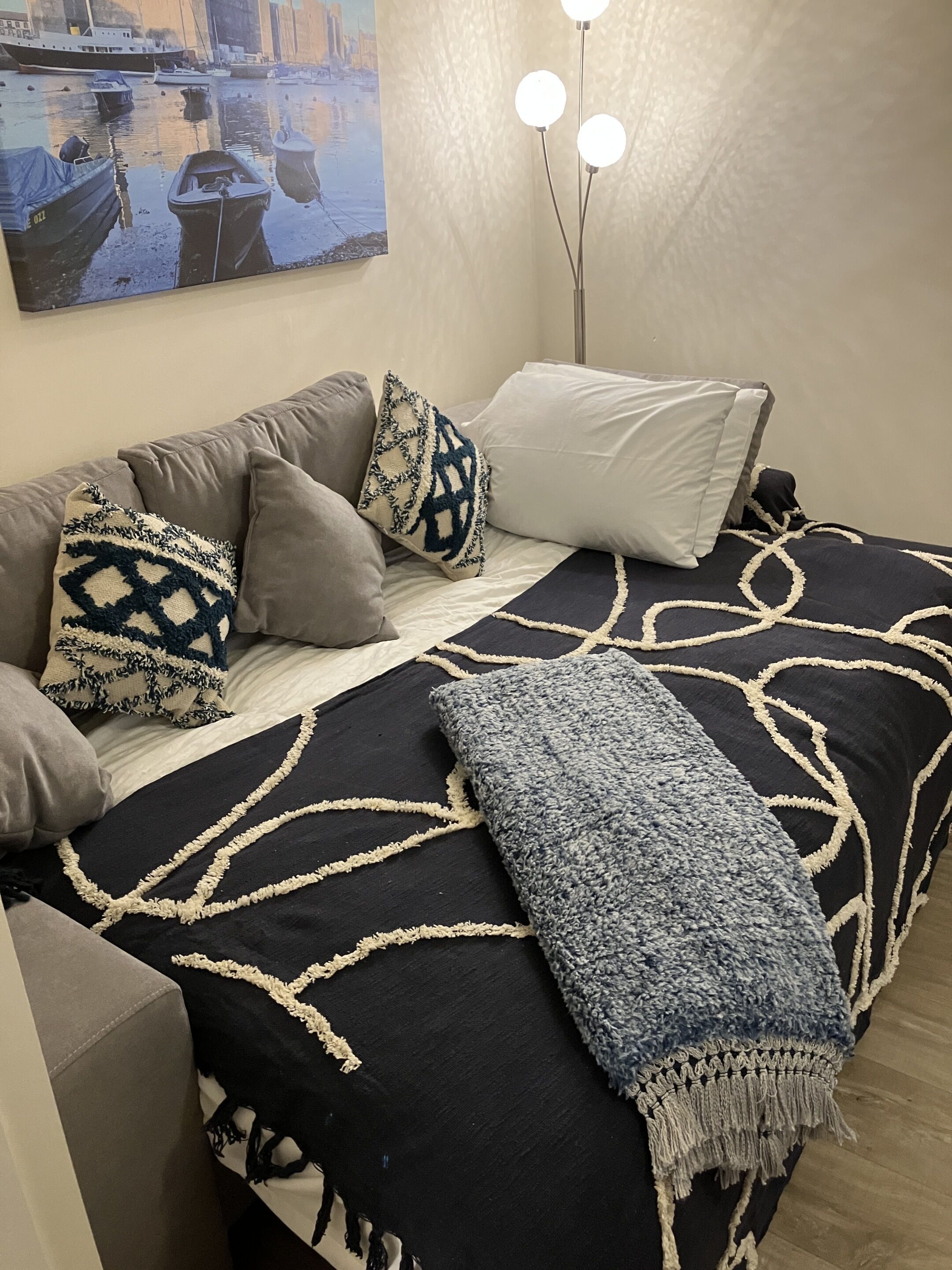 A bedroom with a bed, pillows, a throw blanket, a painting, and a floor lamp.