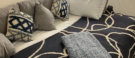 A bedroom with a bed, pillows, a throw blanket, a painting, and a floor lamp.