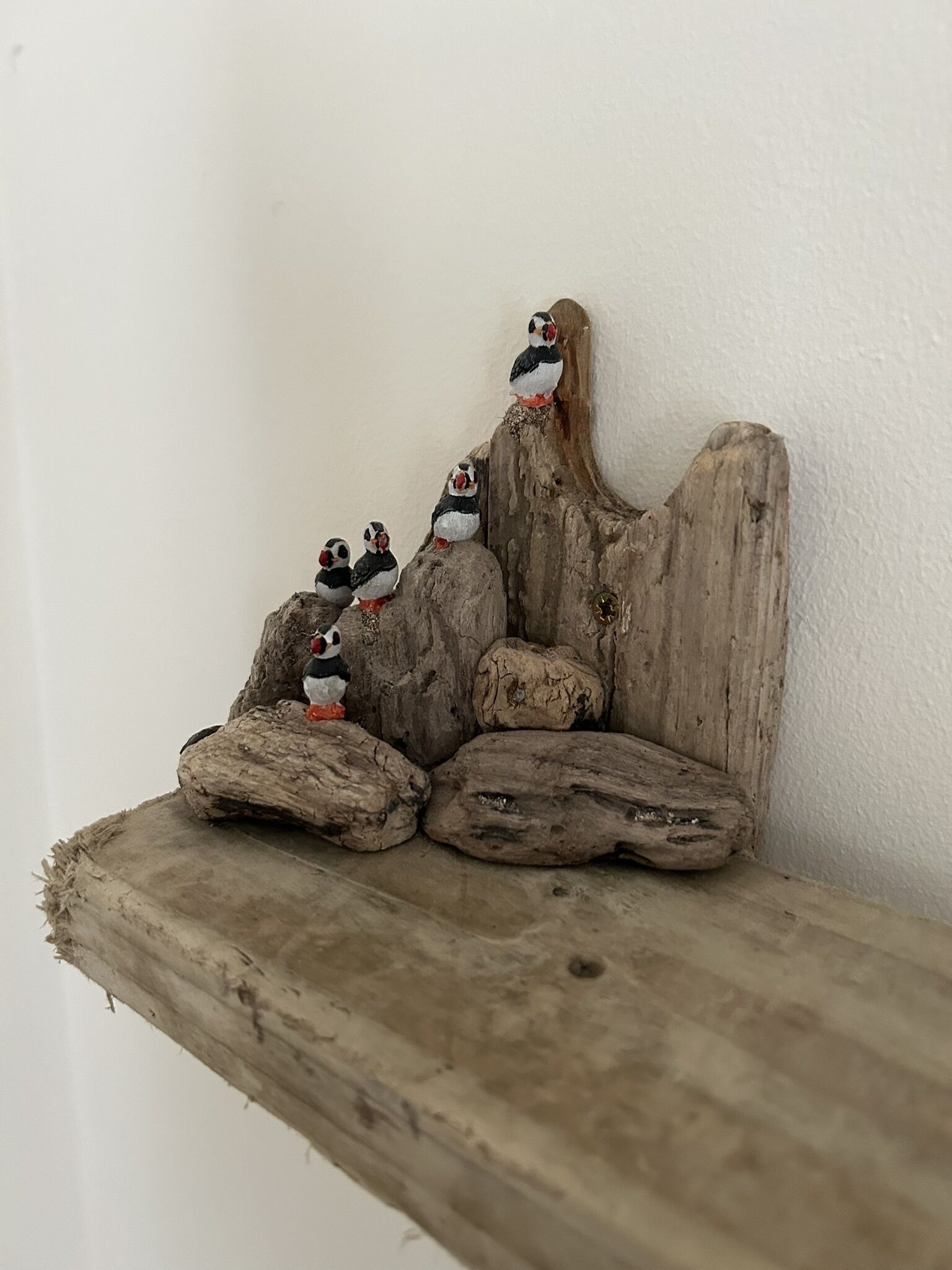 Een houten plank met een rustieke uitstraling, waarop een reeks kleine figuurtjes van pinguïns op een rotsformatie staan.