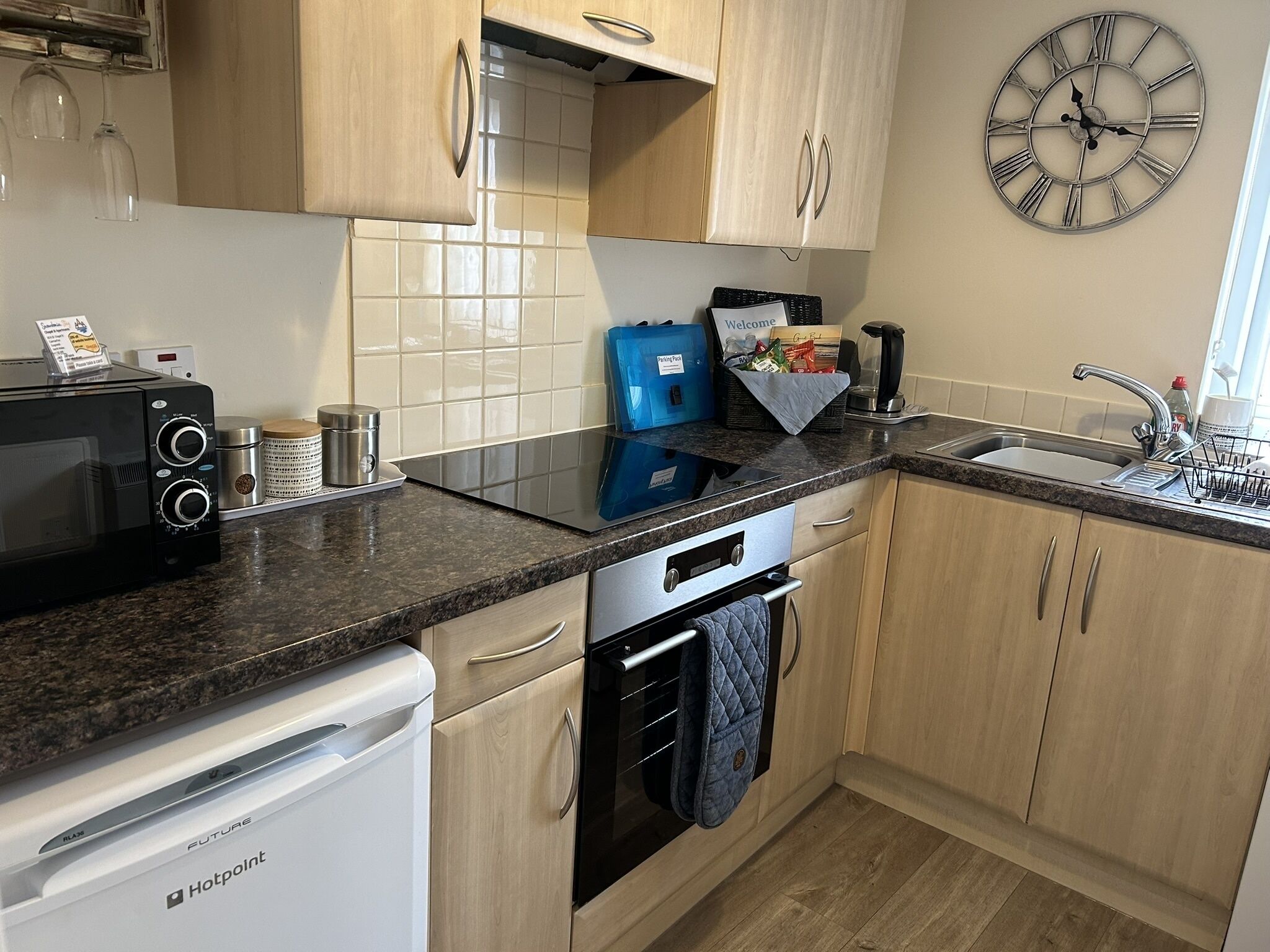 A modern kitchen with a built-in microwave, toaster, and dishwasher. There is a clock on the wall and a welcome sign.