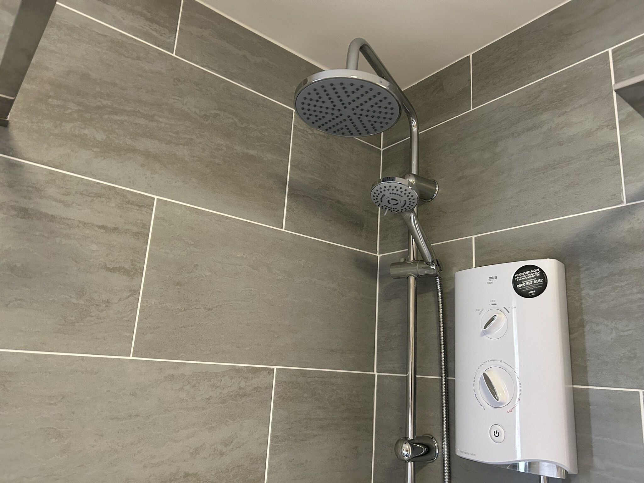 Une douche moderne dotée d’un pommeau de douche à main et d’un panneau de commande fixé au mur.