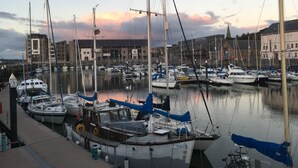 A marina with various boats docked, a building in the background, and a clear sky. - Chapel St Apartments (Caernarfon)