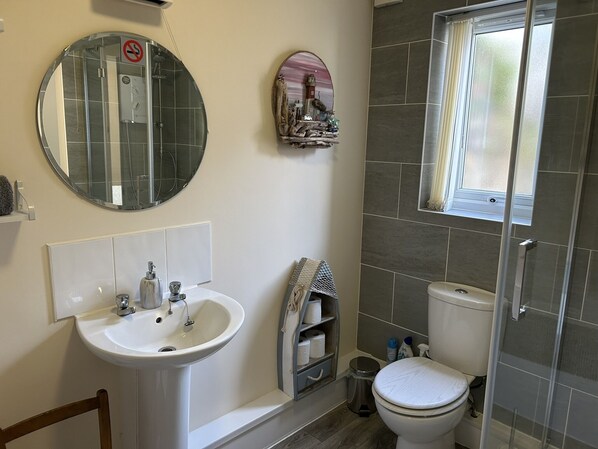 A bathroom with a round mirror, a sink, a toilet, and a shower enclosure. - Chapel St Apartments (Caernarfon)