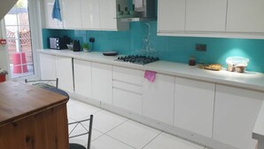 A kitchen with white cabinets, a gas stove, and a window with a view of a red barrel outside. - Amazing Ilford 3 bedroom house (Ilford)