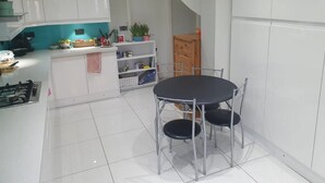 A modern kitchen with white cabinets, a black dining table, and a small island with a sink. - Amazing Ilford 3 bedroom house (Ilford)