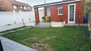 A backyard with a red wooden shed, a white fence, and a paved patio area. - Amazing Ilford 3 bedroom house (Ilford)