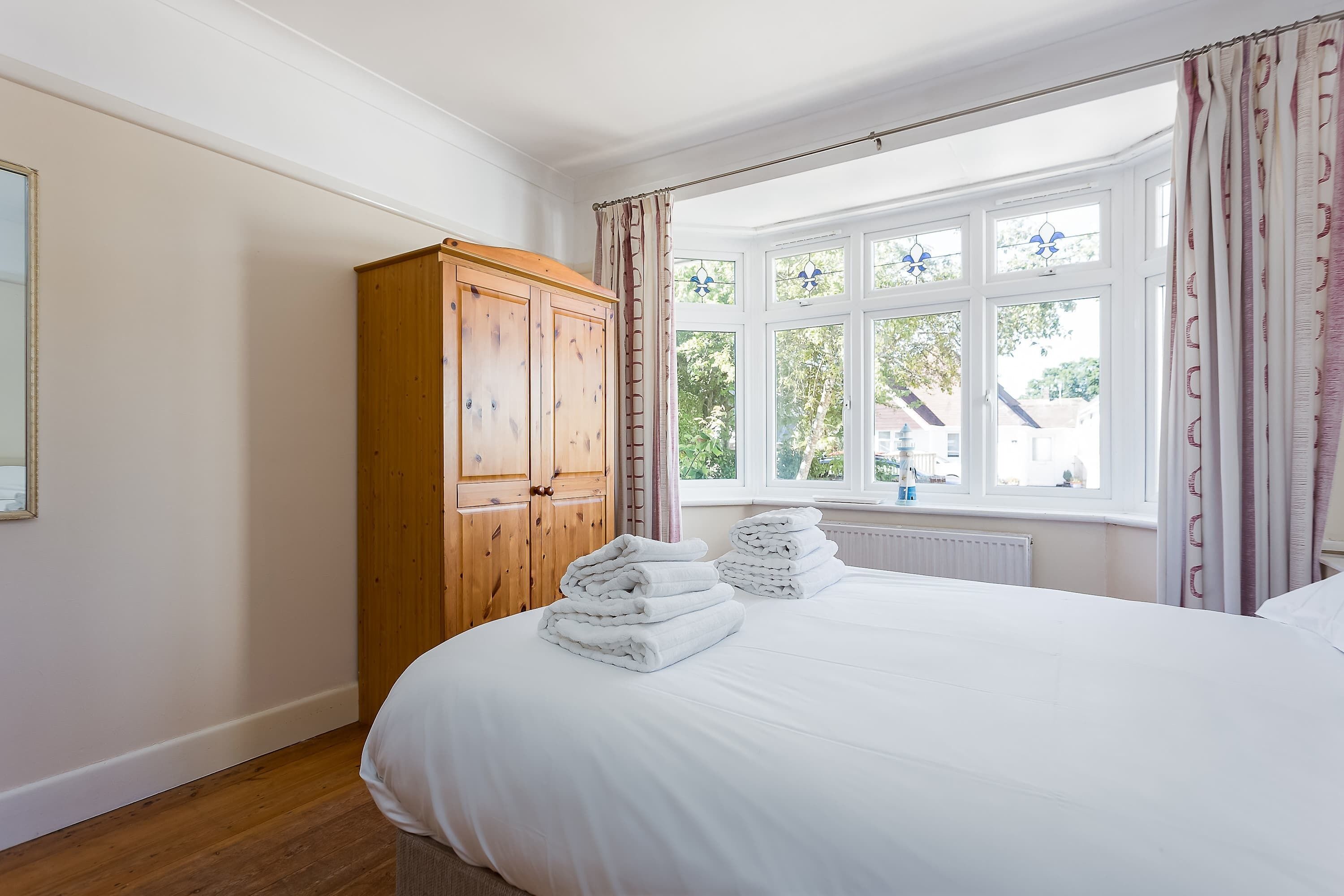 A bedroom with a large bed, a wooden wardrobe, and a window with curtains.