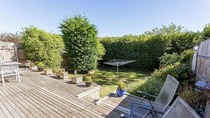 Een houten terras met tuinmeubilair, plantenpotten en een metalen parasol.