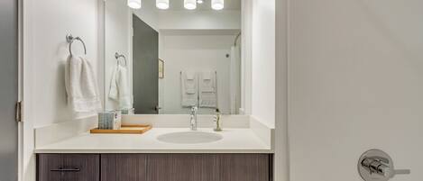 A modern bathroom with a large mirror, a sink, and a vanity with drawers.