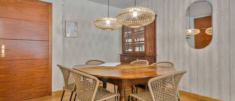 Un comedor con mesa de madera, sillas de mimbre, un armario de madera y un espejo en la pared.